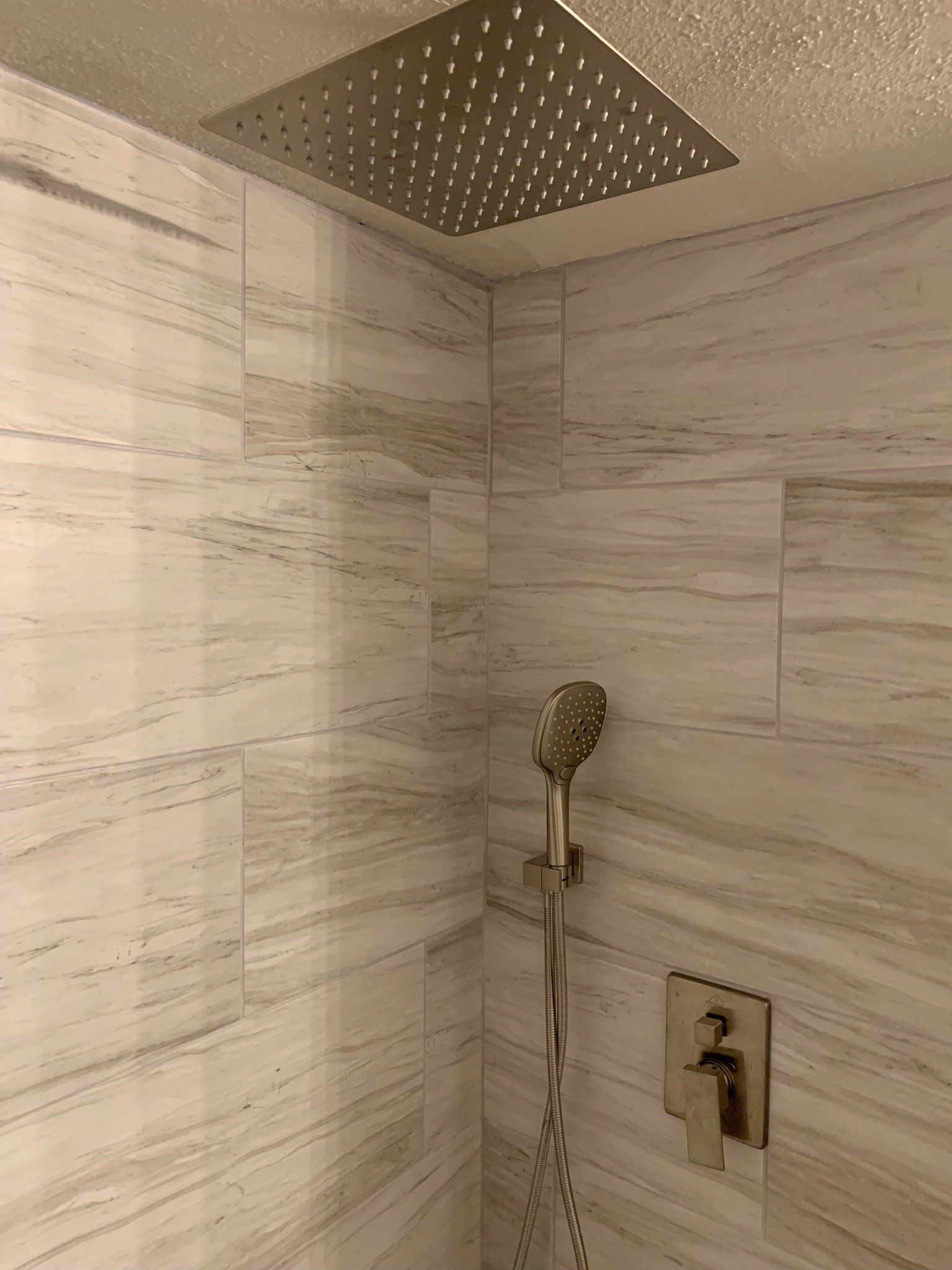 A shower with a square shower head and a handheld shower head.