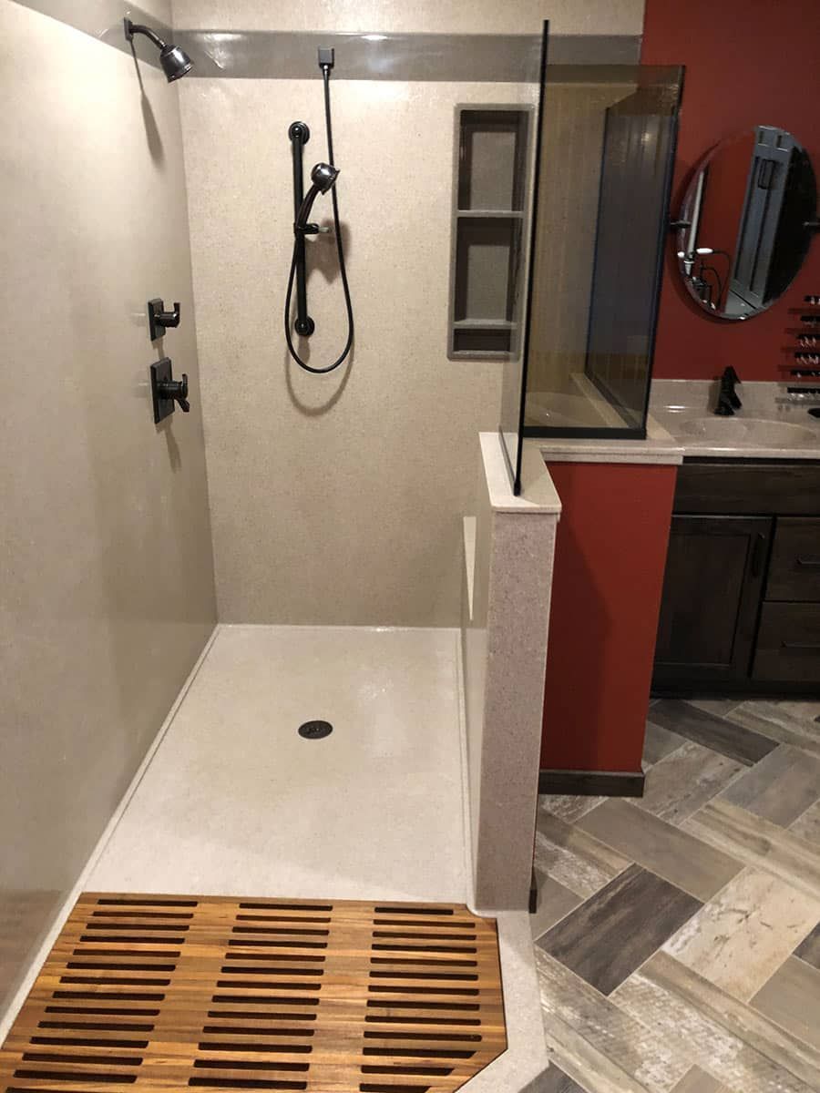 Modern bathroom with a walk-in shower, wooden floor mat, and glass partition. Red and beige tones.