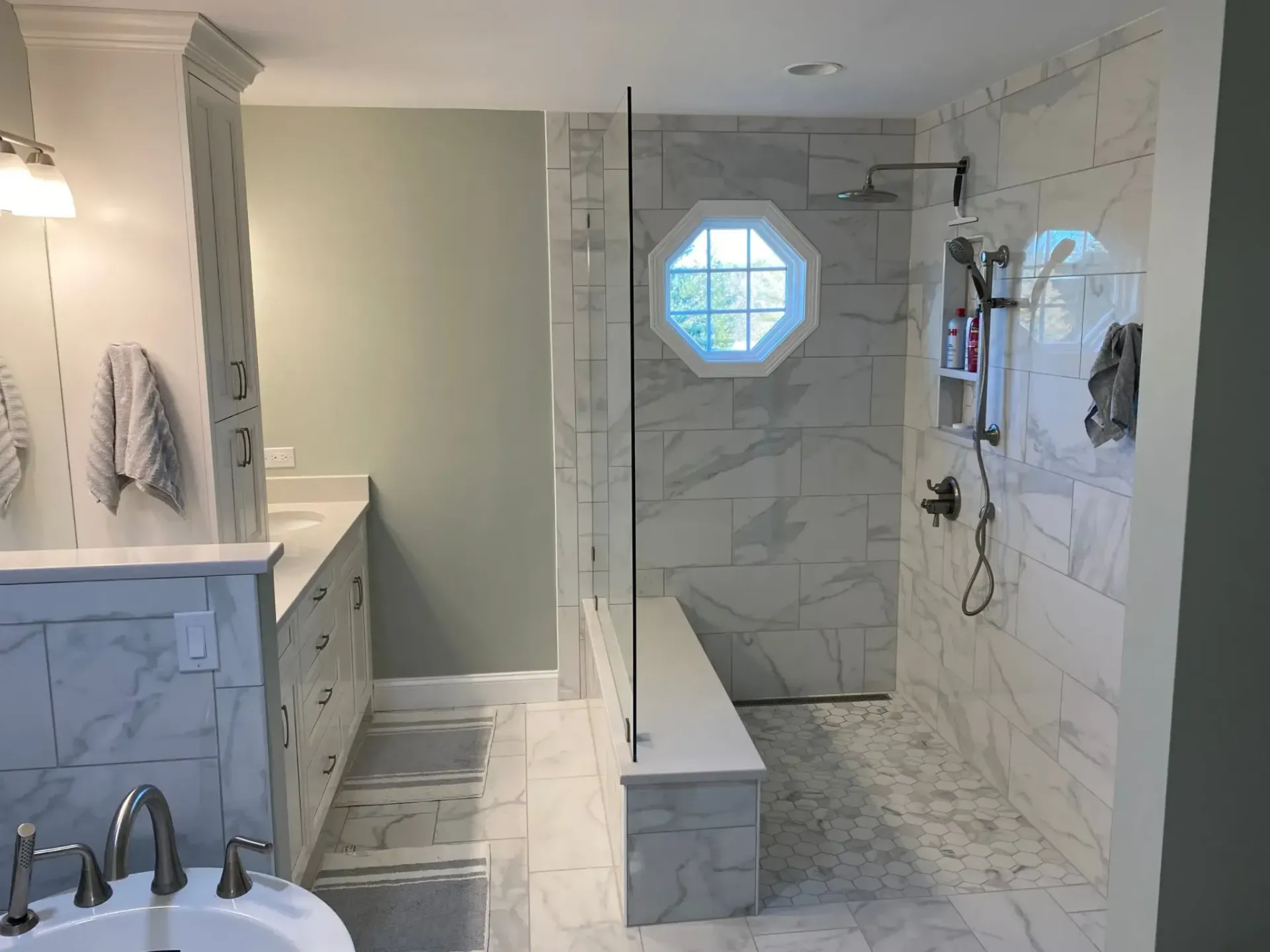 Bathroom with white marble tile and glass shower, light green wall, and an octagonal window.