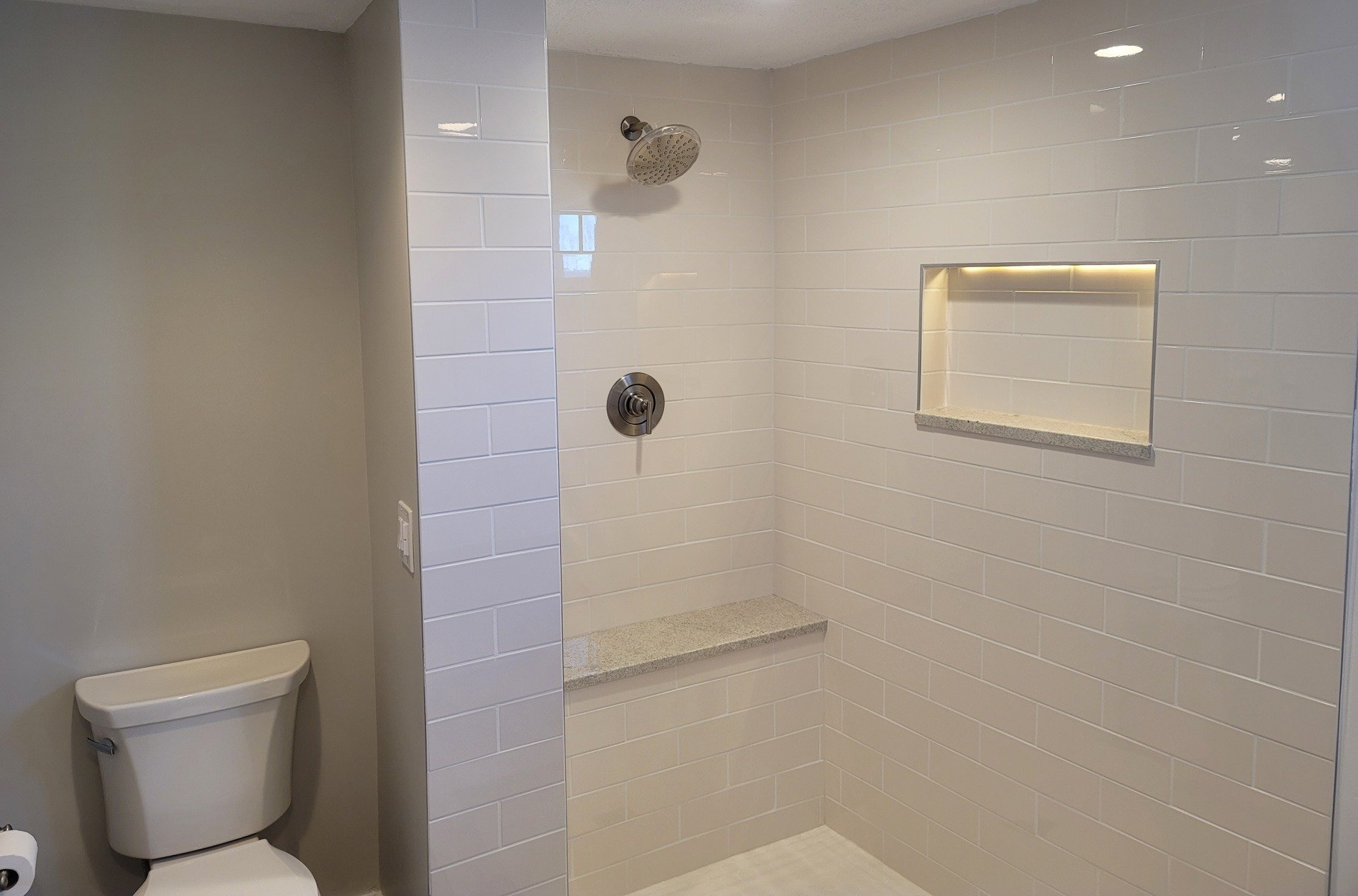 A newly tiled walk-in shower with navy blue and white tiles, a built-in bench, and a recessed shelf.