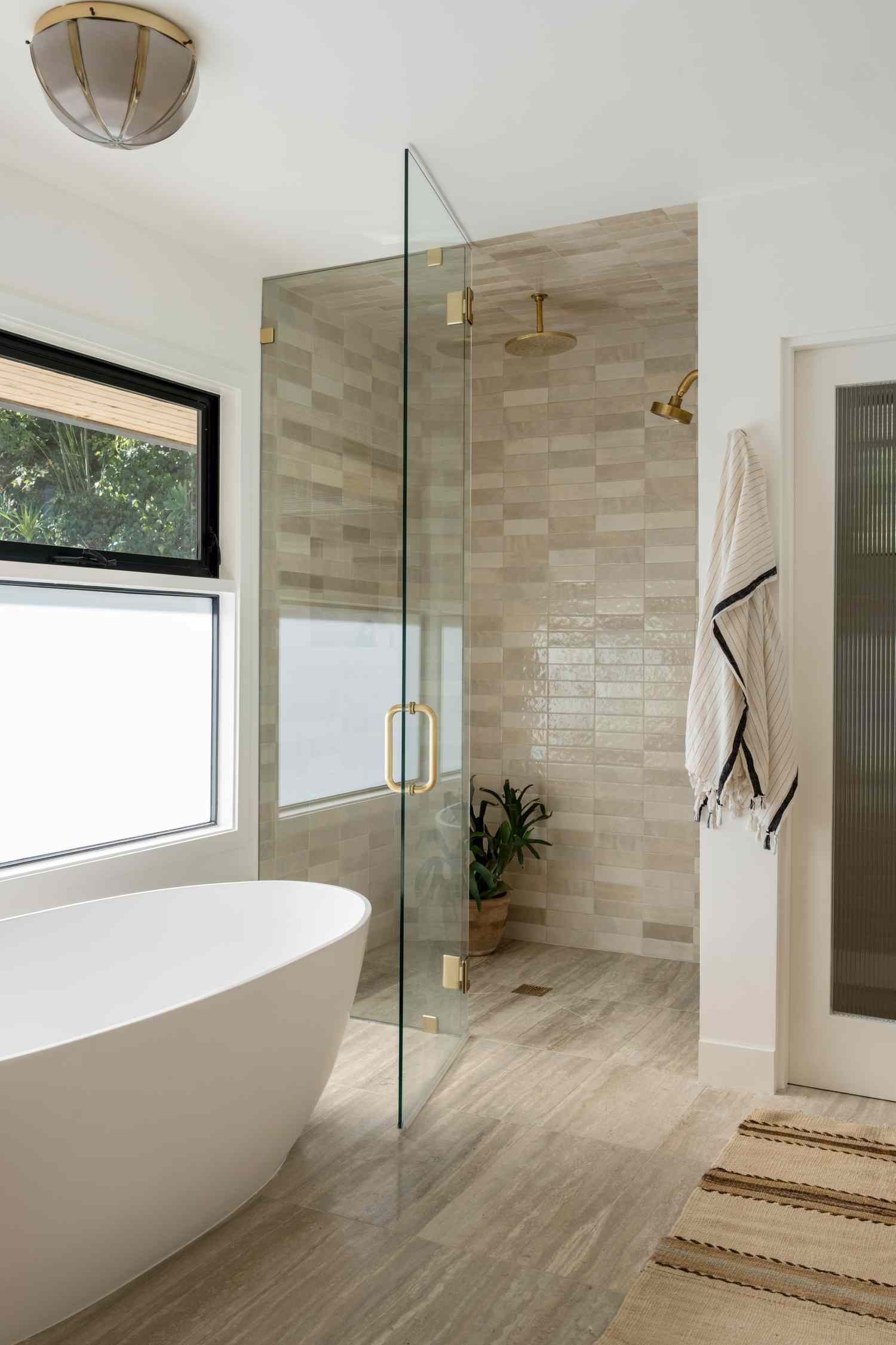 Modern bathroom with glass shower, freestanding tub, and neutral tile.