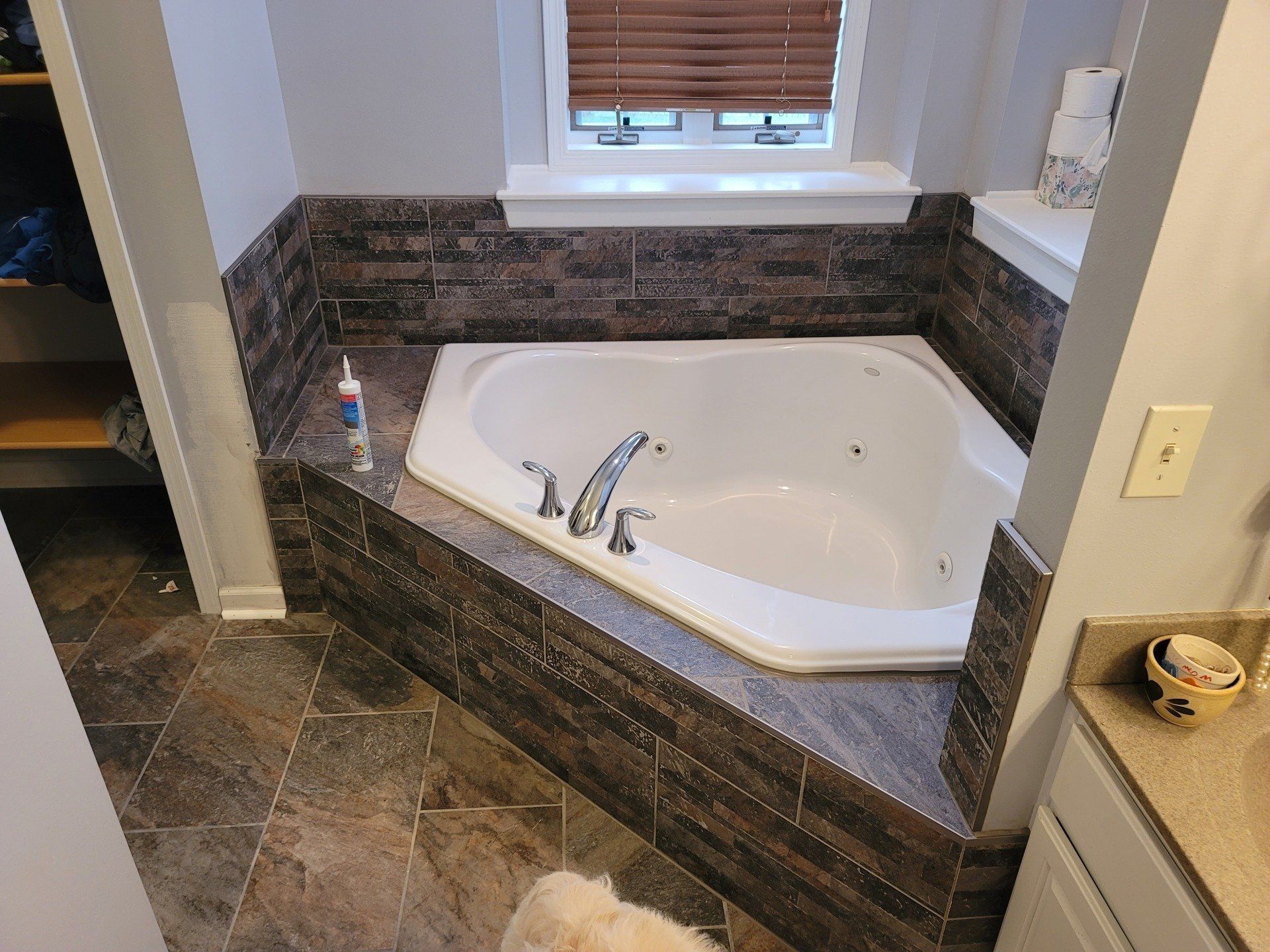 Bathroom with a corner jacuzzi tub, brown tile surround, and brown tiled floor.