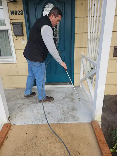 A man is using a pressure washer to clean a porch