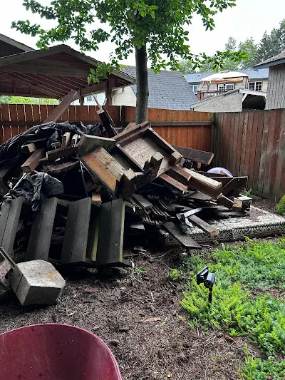 A pile of trash is sitting in a backyard next to a wooden fence.