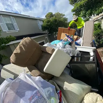 A man is loading a truck full of furniture into a dumpster.