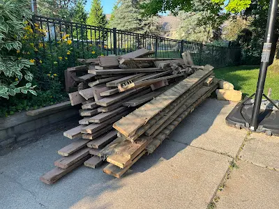 A pile of wood is sitting on the sidewalk next to a fence.