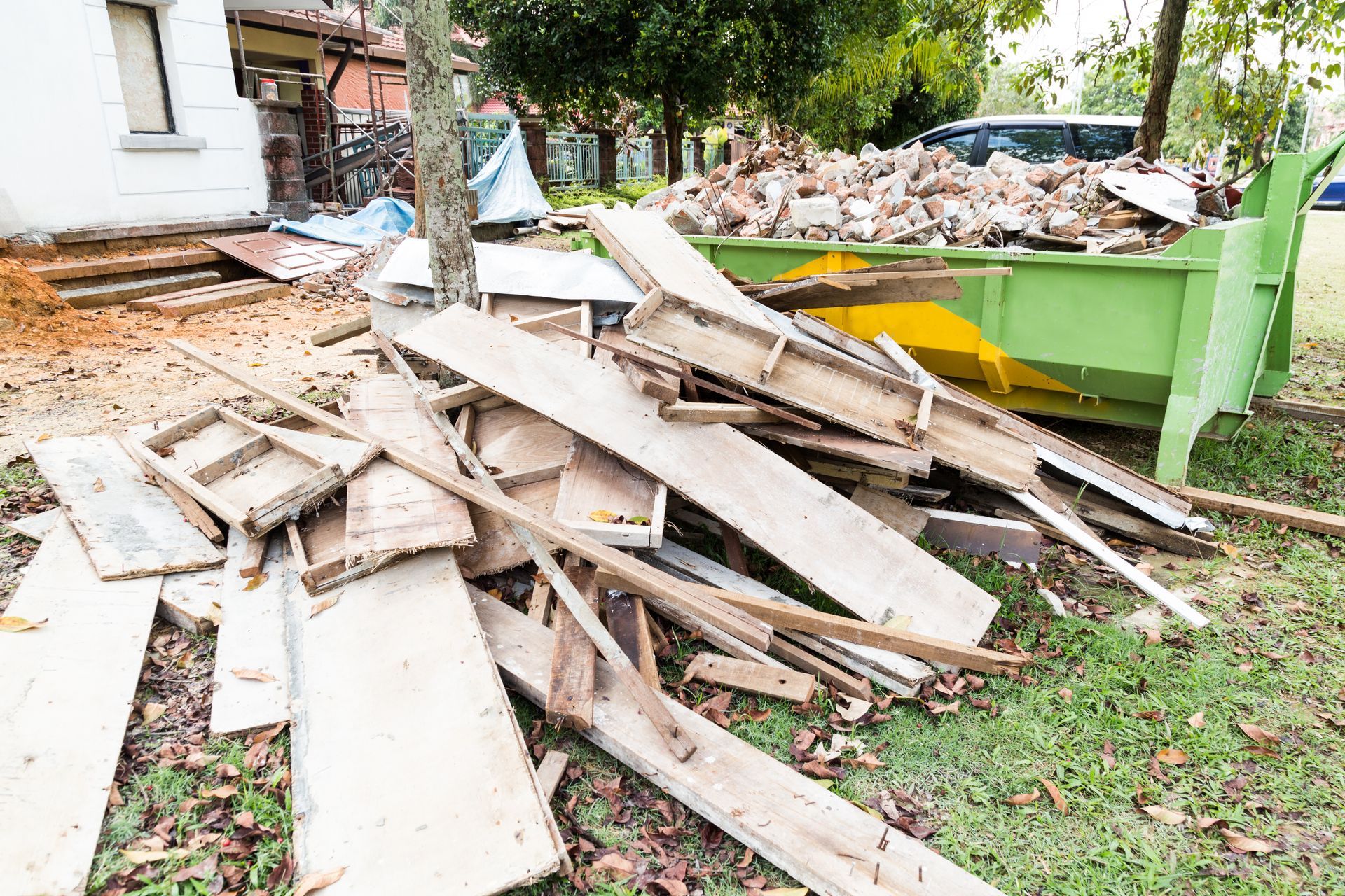 A pile of wood is sitting in front of a green dumpster.