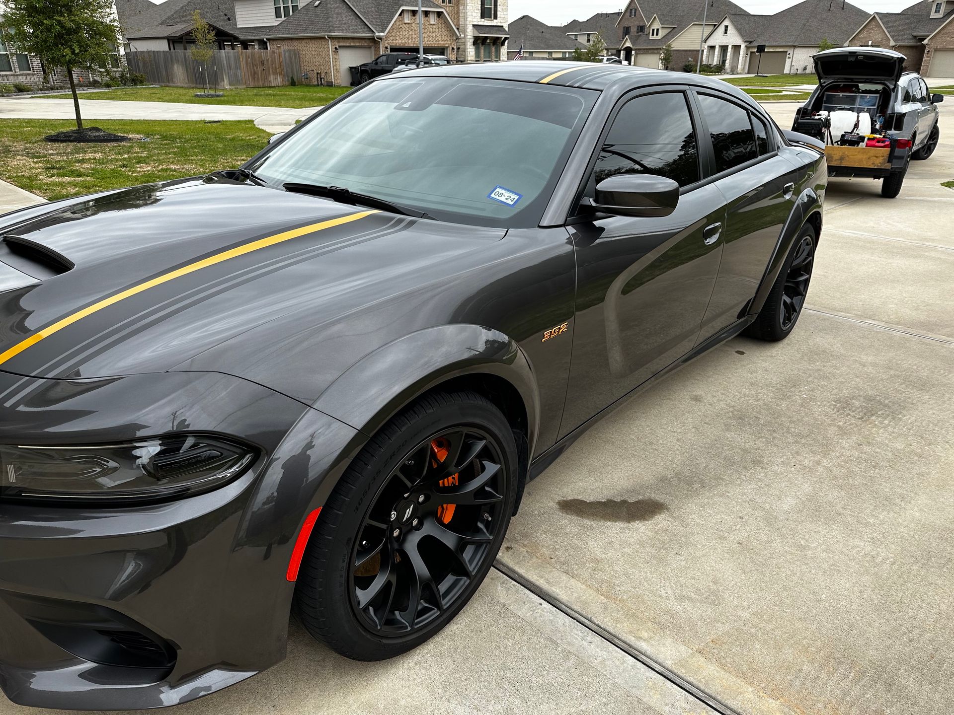 A black dodge charger with a yellow stripe on the hood is parked in a driveway.