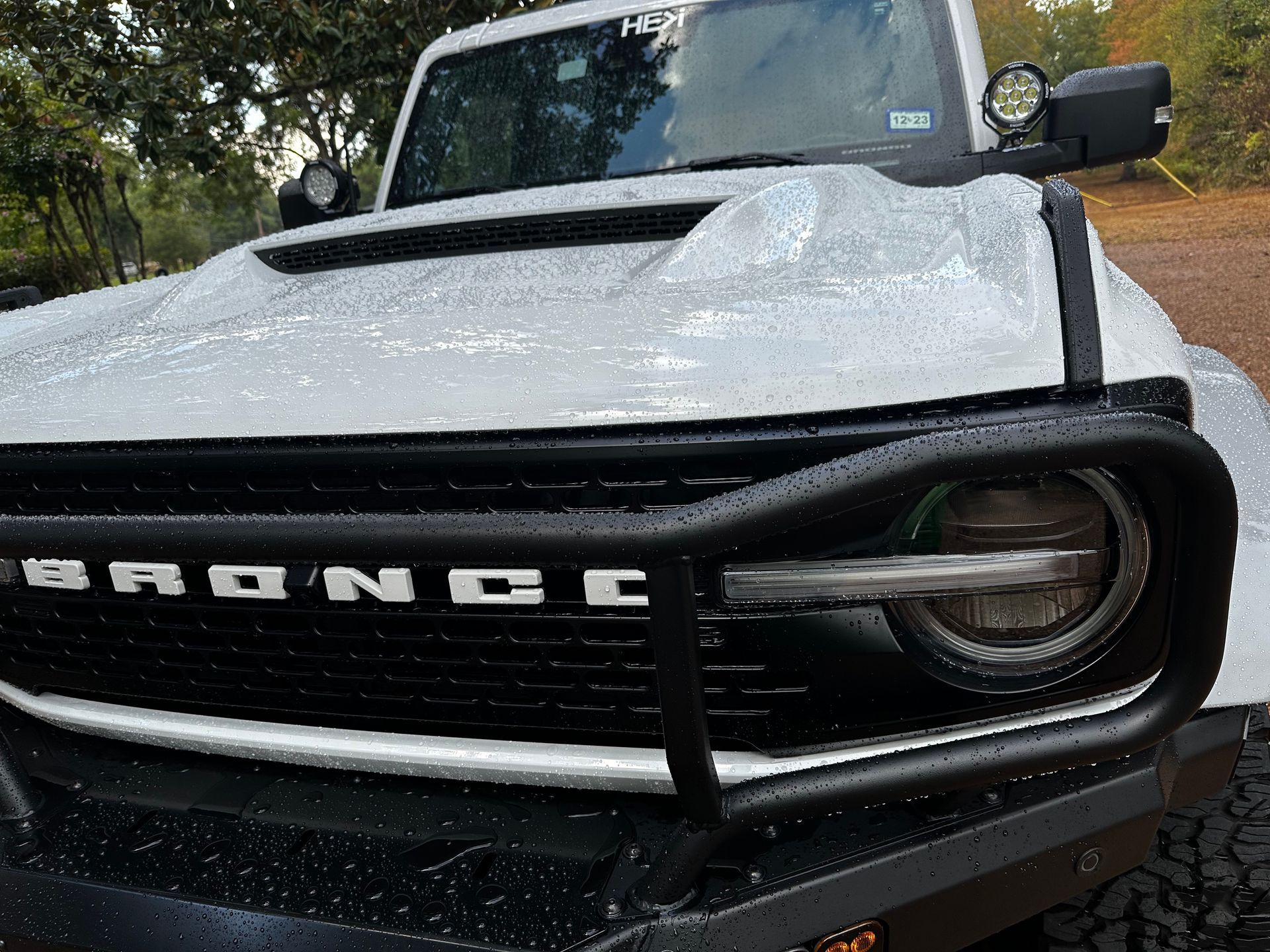 A white ford bronco is parked in the rain on a dirt road.