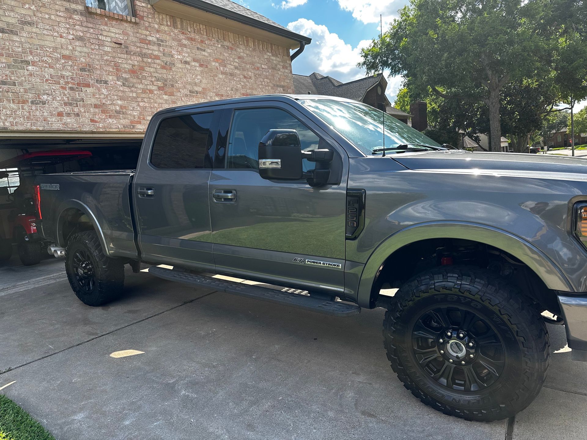 A gray truck is parked in a driveway in front of a brick house.