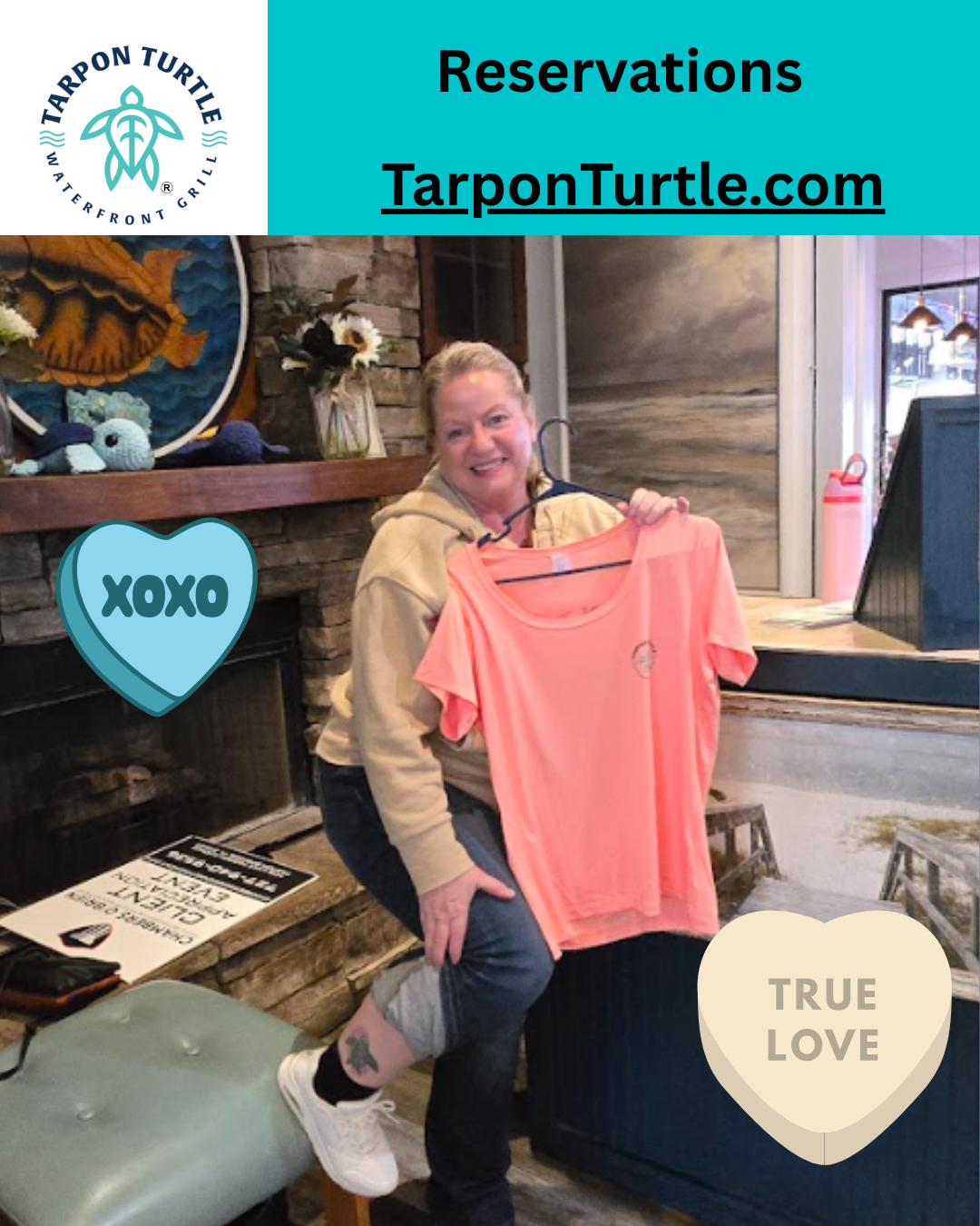 A woman holding an orange t-shirt in front of a fireplace, with digital 