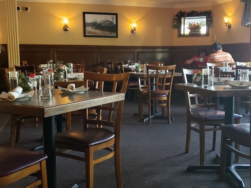 A restaurant with tables and chairs and a man sitting in the corner