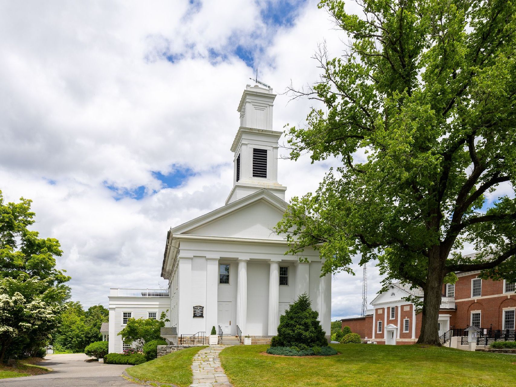 A white church with a clock tower and a tree in front of it
