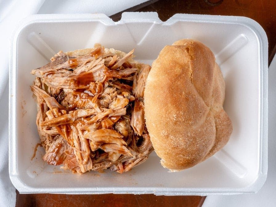 A styrofoam container filled with pulled pork and a roll.