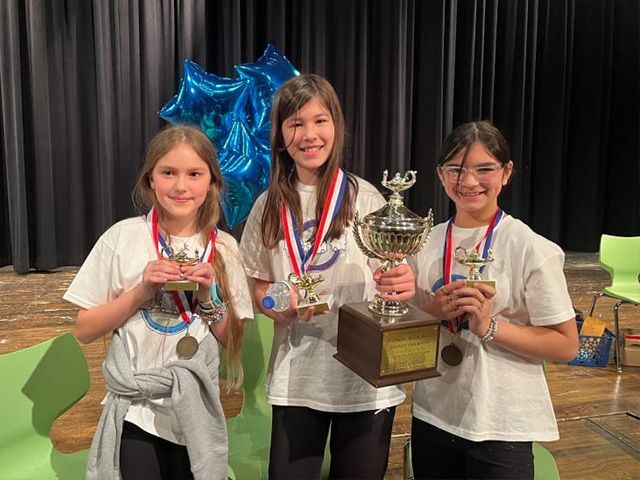 Three young girls are standing next to each other holding trophies and medals.