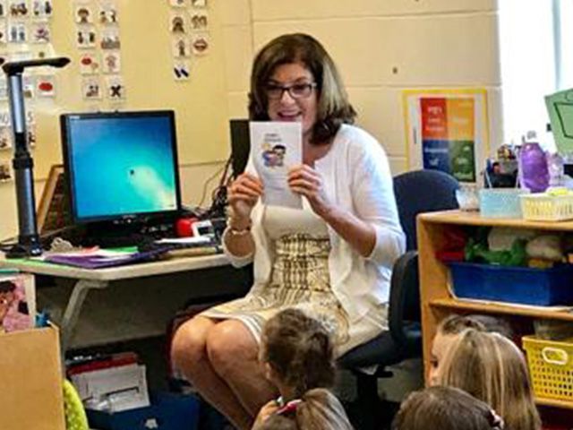 A woman is reading a book to a group of children in a classroom