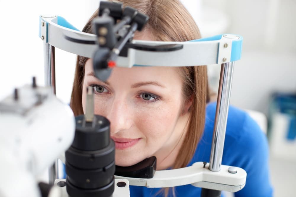 A Woman in a Blue Shirt Undergoes an Eye Exam at an Optometrist's Office, Using a Slit Lamp