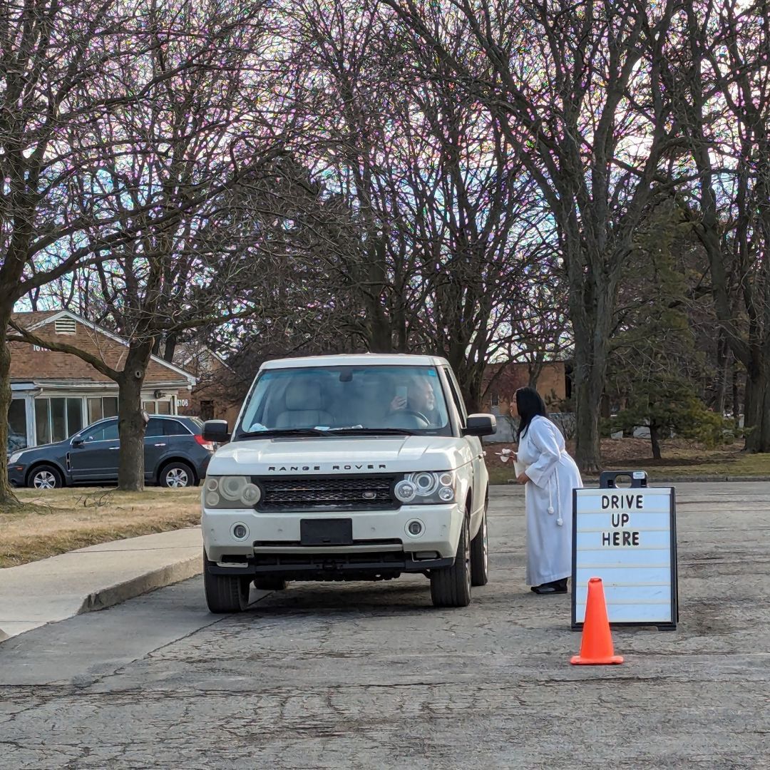 Deb Davis standing car side, during Ash Wednesday, praying with and giving ashes to driver, in white SUV.