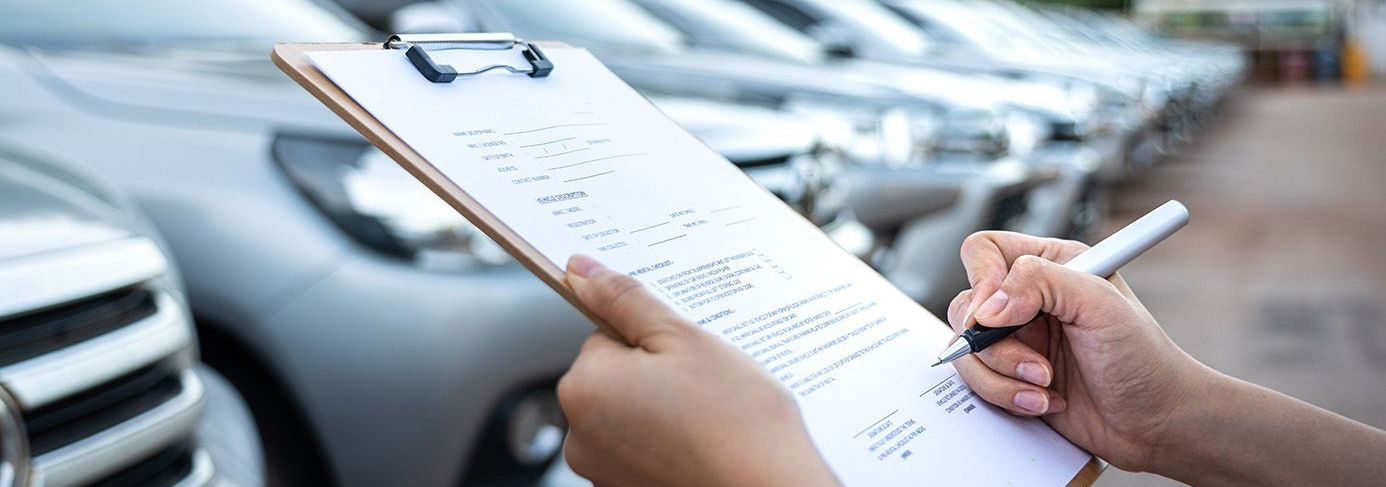 a person is writing on a clipboard in front of a row of cars .