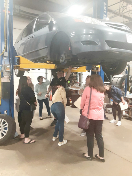 A group of people looking at a car on a lift in a garage
