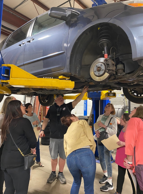 A group of people are looking under a car on a lift