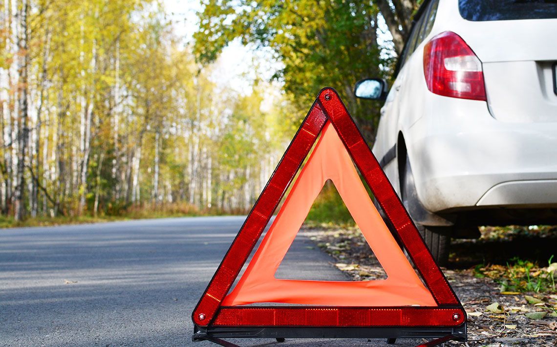 A white car is parked next to an orange triangle on the side of the road