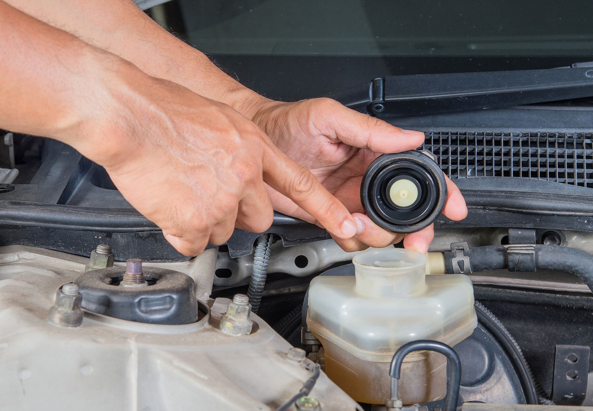 A person is holding a cap over a brake fluid reservoir in a car.