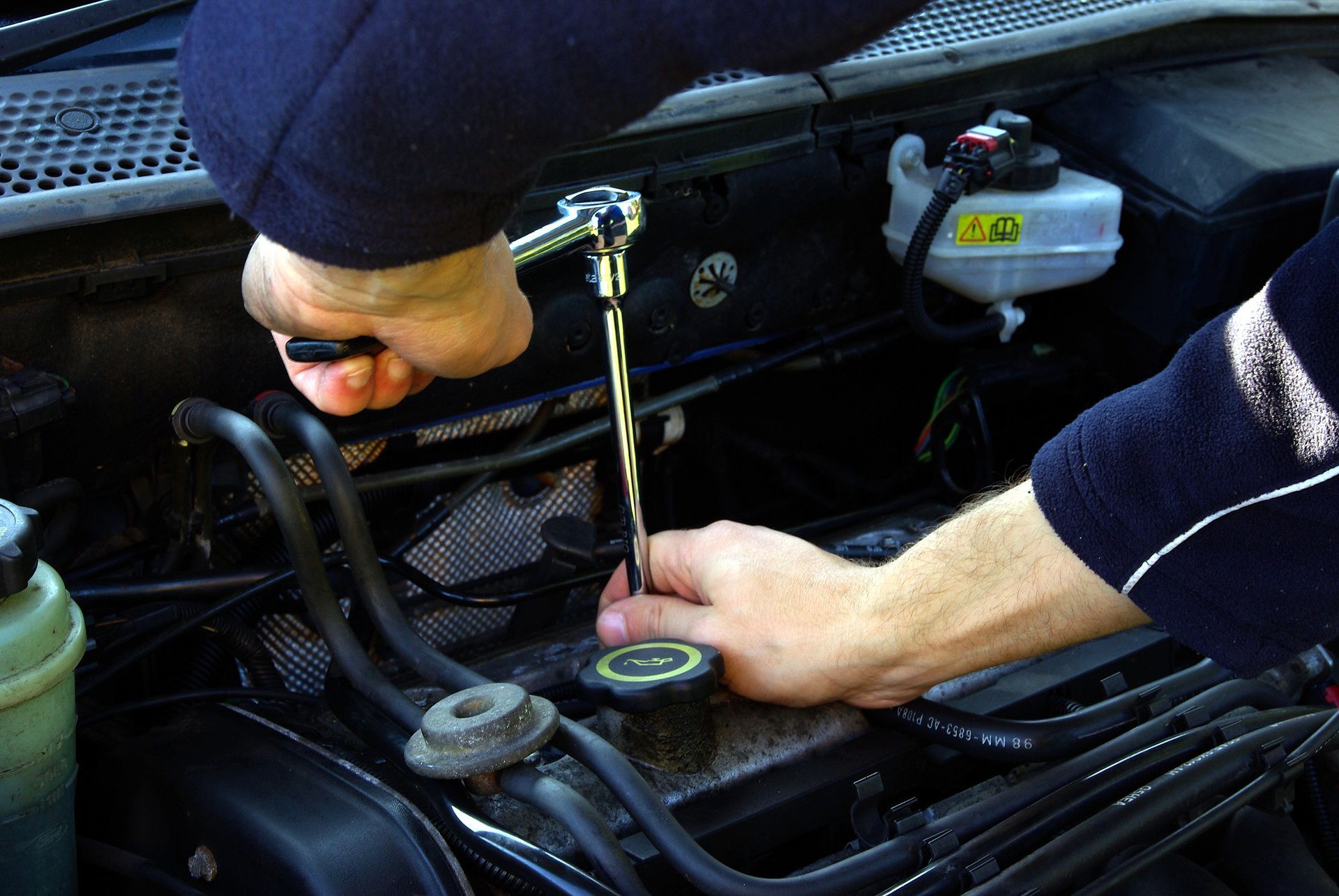 A man is working on a car engine with a wrench.