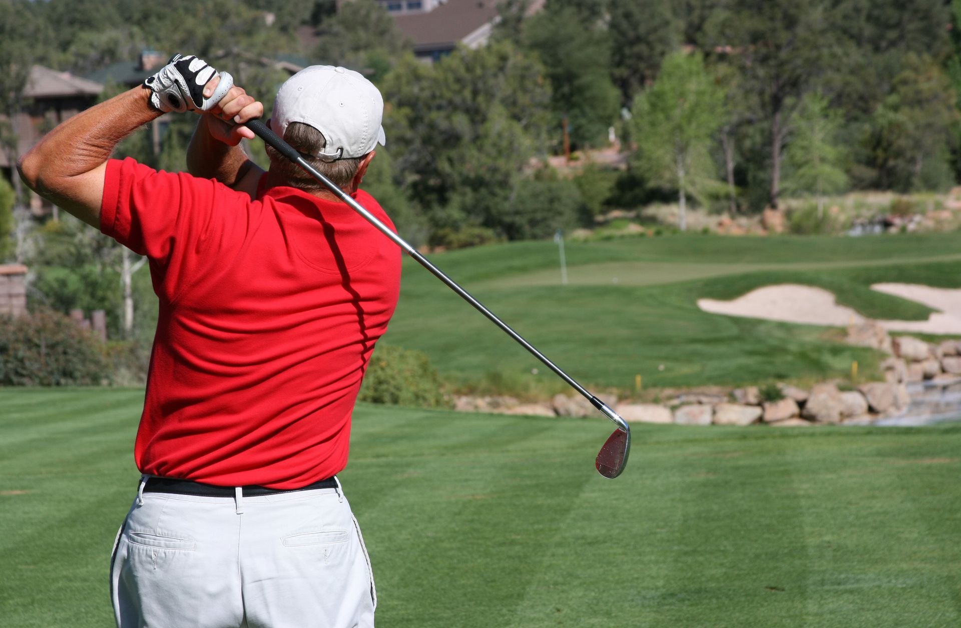 A man in a red shirt is swinging a golf club on a golf course.