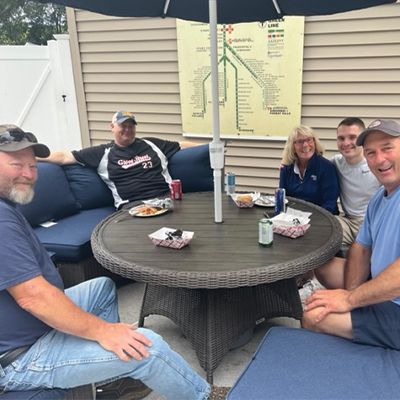a group of people are sitting around a table under an umbrella