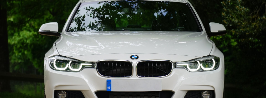 a white bmw is parked in front of a forest .