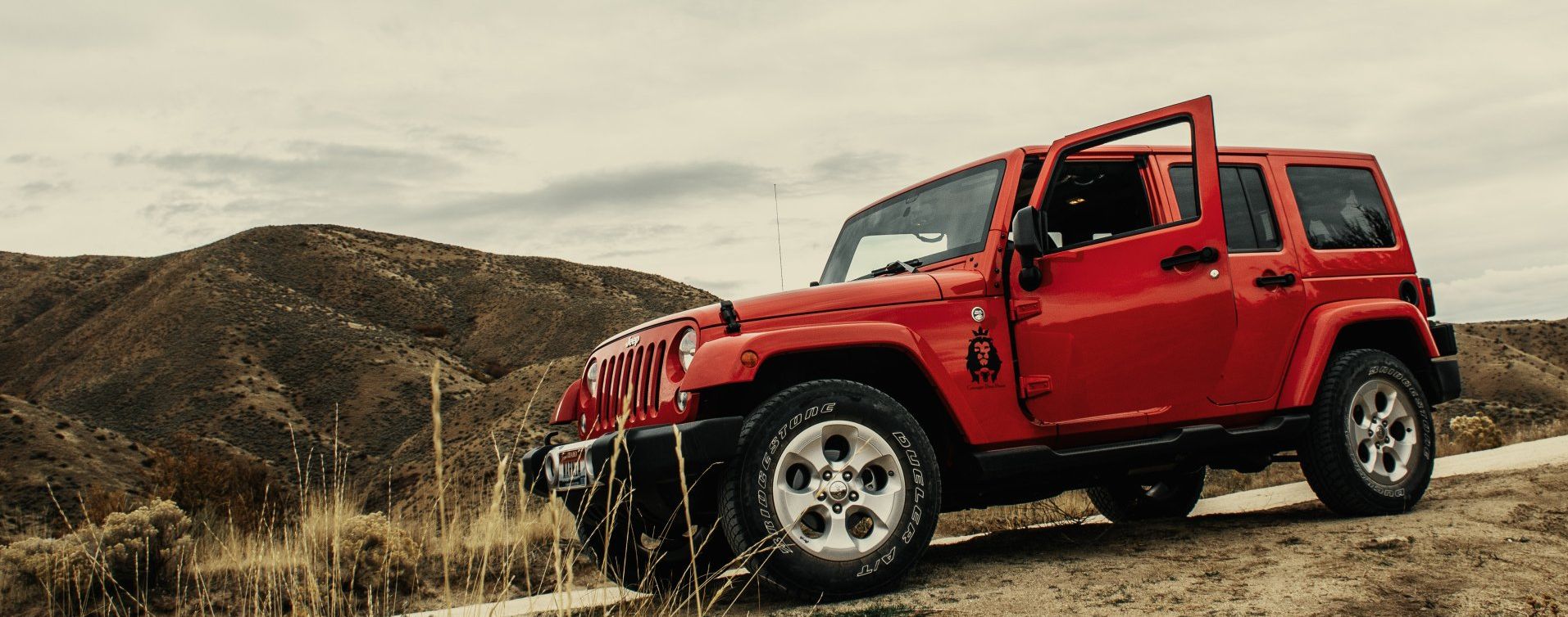 a red jeep is parked on the side of a dirt road .