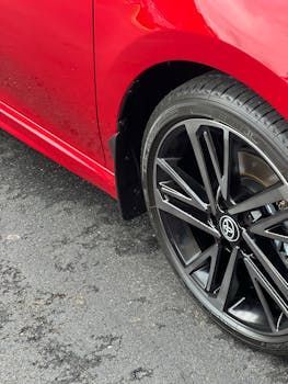 Red car with a black wheel and tire on a wet asphalt surface.