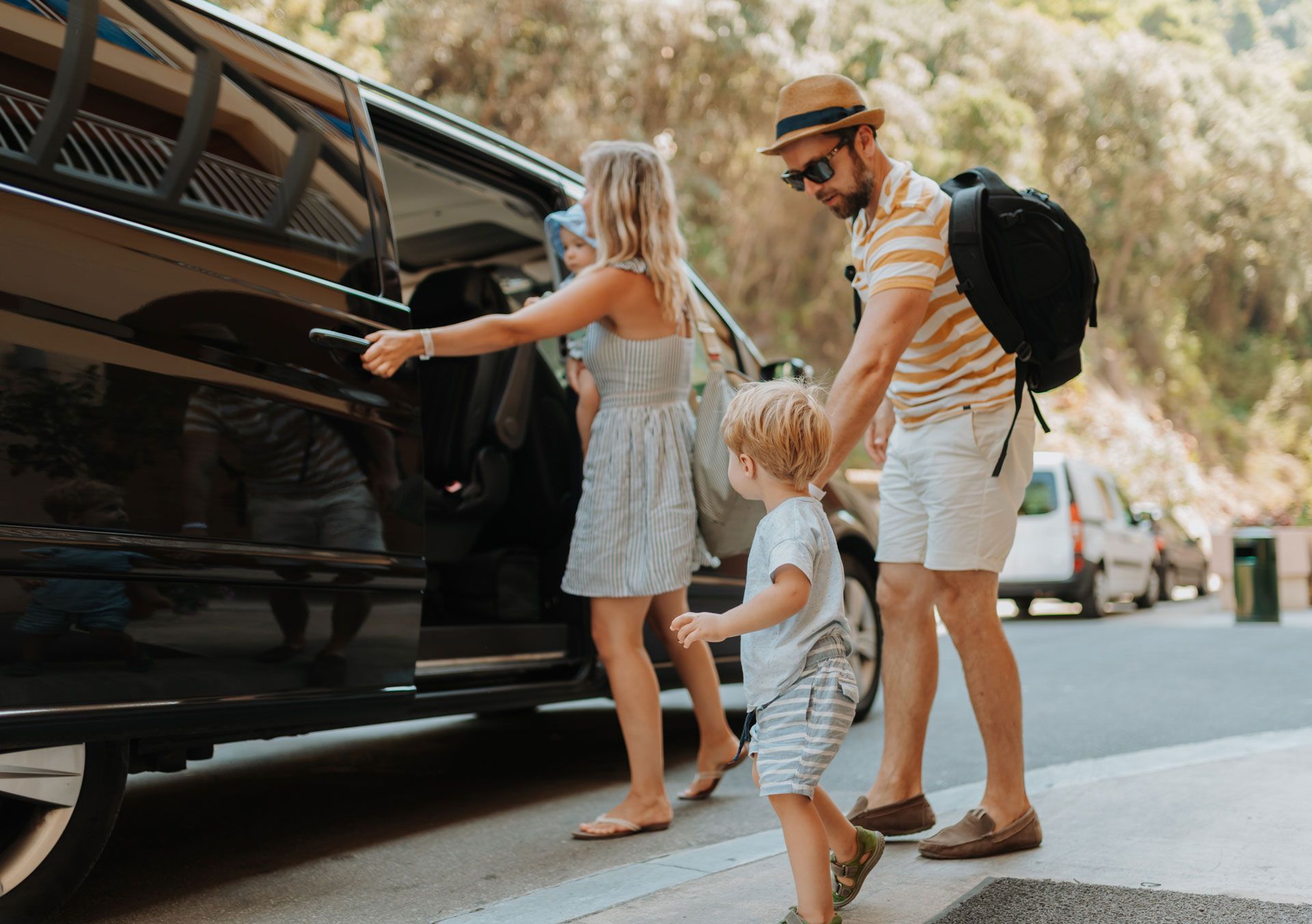Family loading luggage into a black car on a sunny street