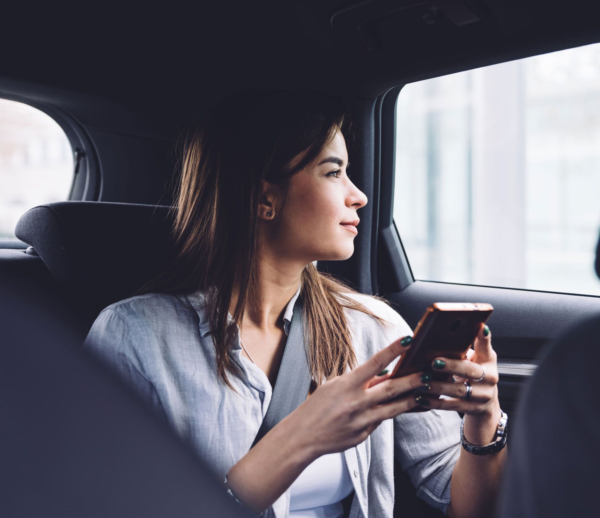 Woman sitting in a car, looking out the window while holding a smartphone