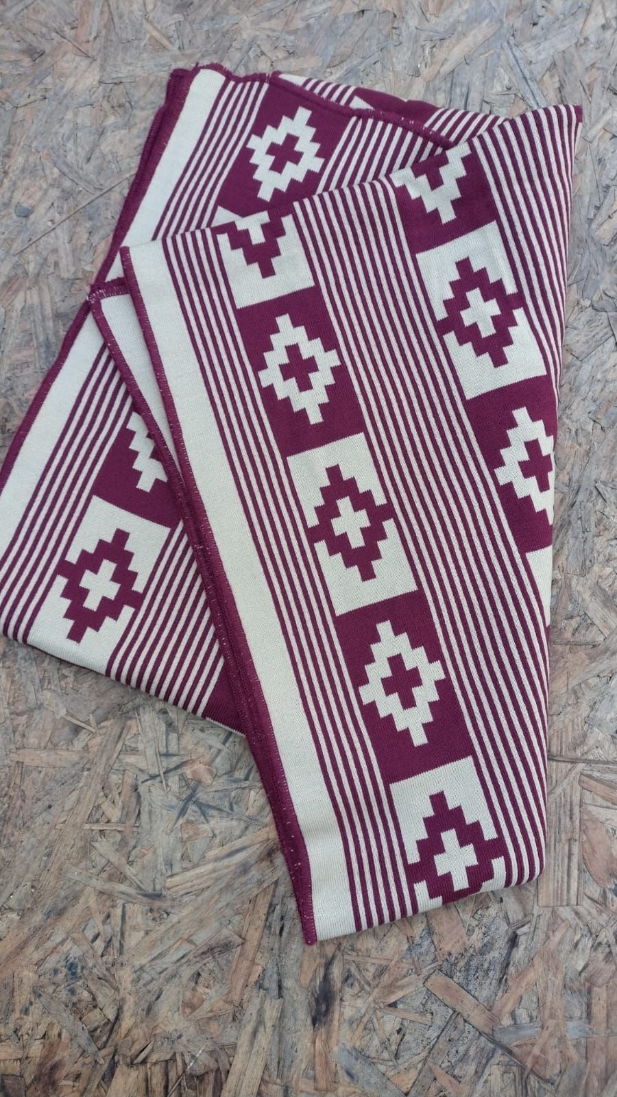 Una manta morada y blanca con un patrón geométrico reposa sobre una superficie de madera.