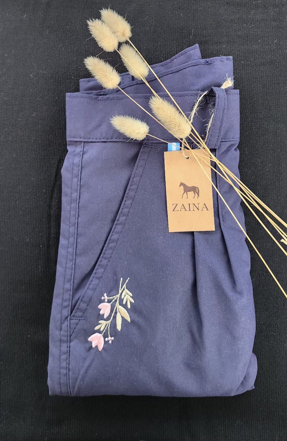 Un par de pantalones morados con flores bordadas y una etiqueta.