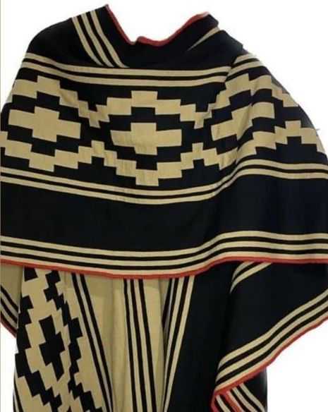 Un poncho de rayas negras y tostadas con un borde rojo.