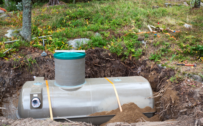 A grey septic tank sitting in a hole in the ground in Coos County
