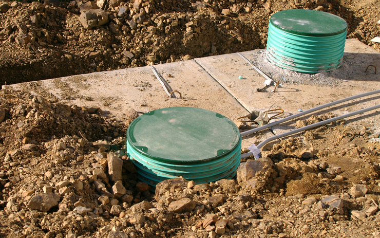 A septic tank buried in the dirt with two green attachments