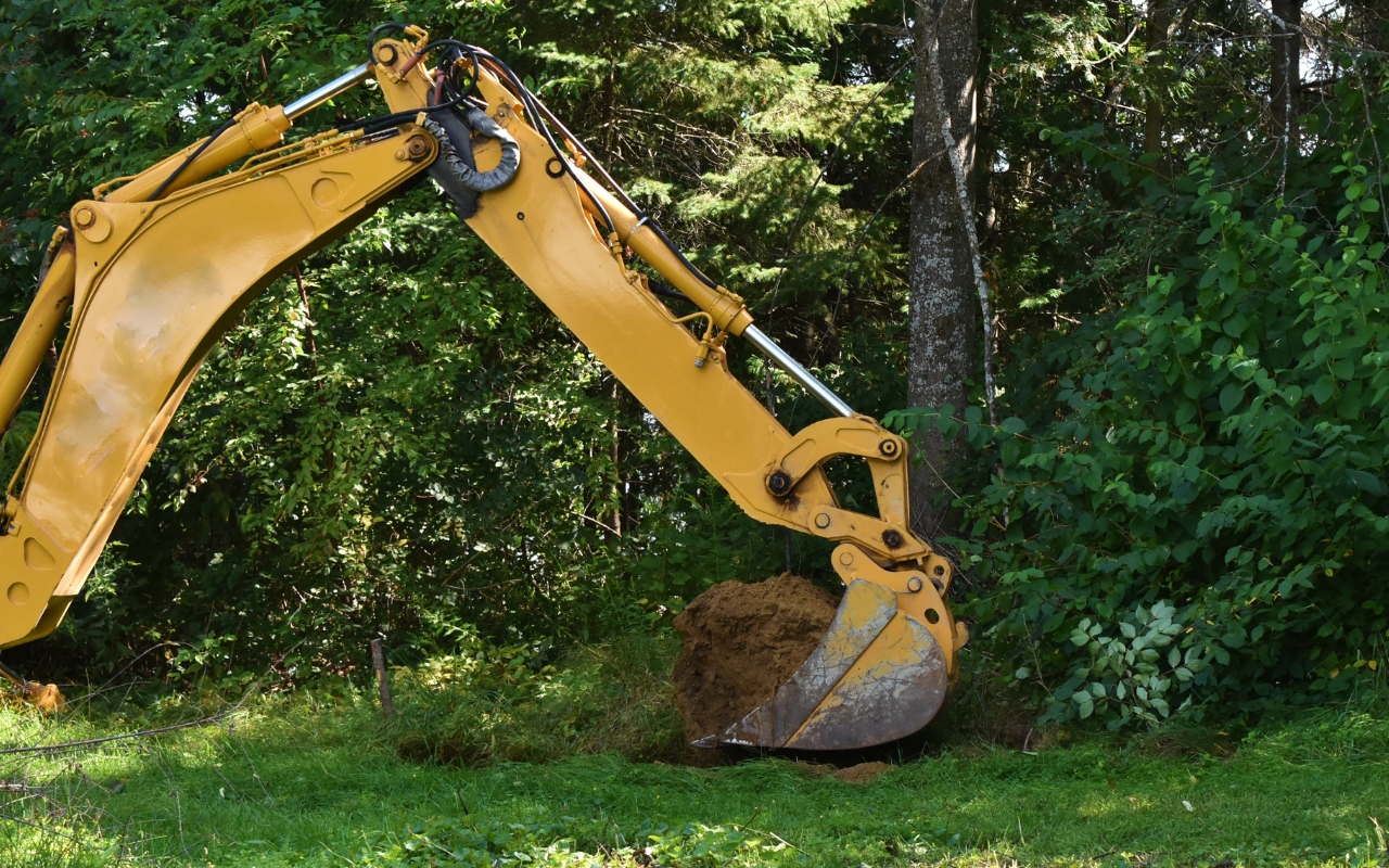 Yellow excavator digging in a grassy area near trees.