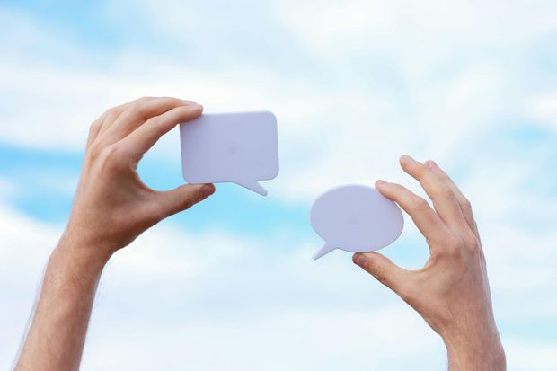 A person is holding two paper speech bubbles in their hands.