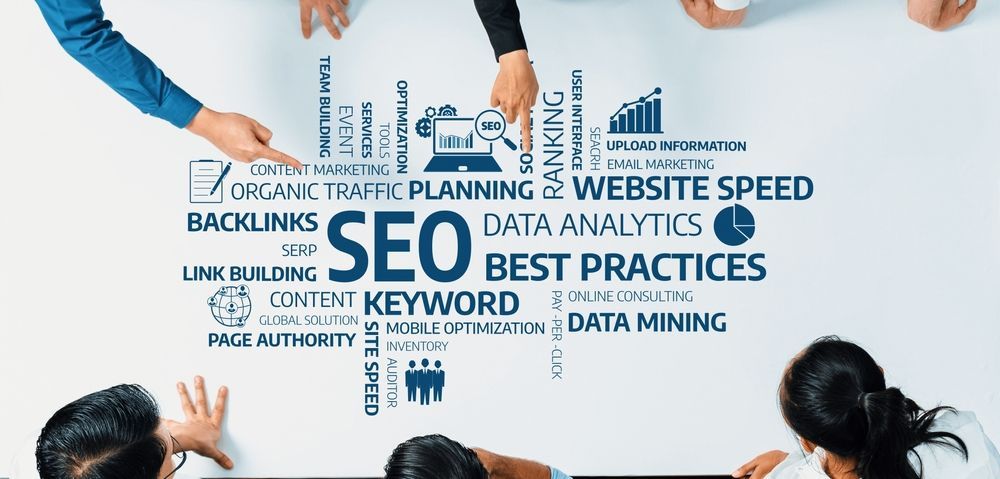 A group of people are sitting around a table with a sign that says seo best practices.