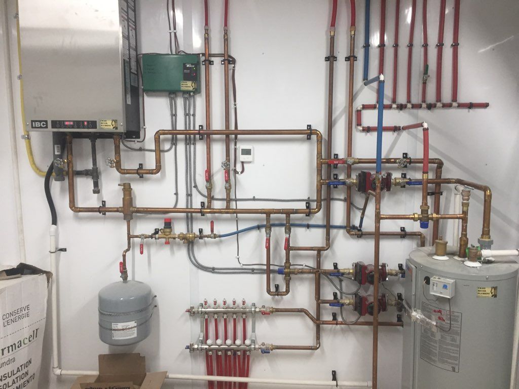 Complex plumbing system with copper pipes, a water heater, and a heating system mounted on a white wall.