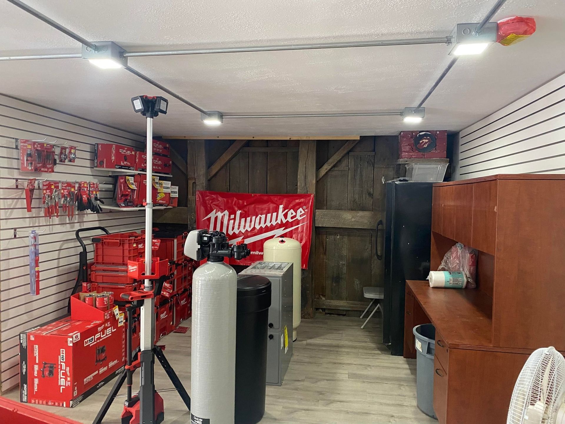 Inside a shop, displaying Milwaukee tools, equipment, and supplies; interior features wood-paneled wall.
