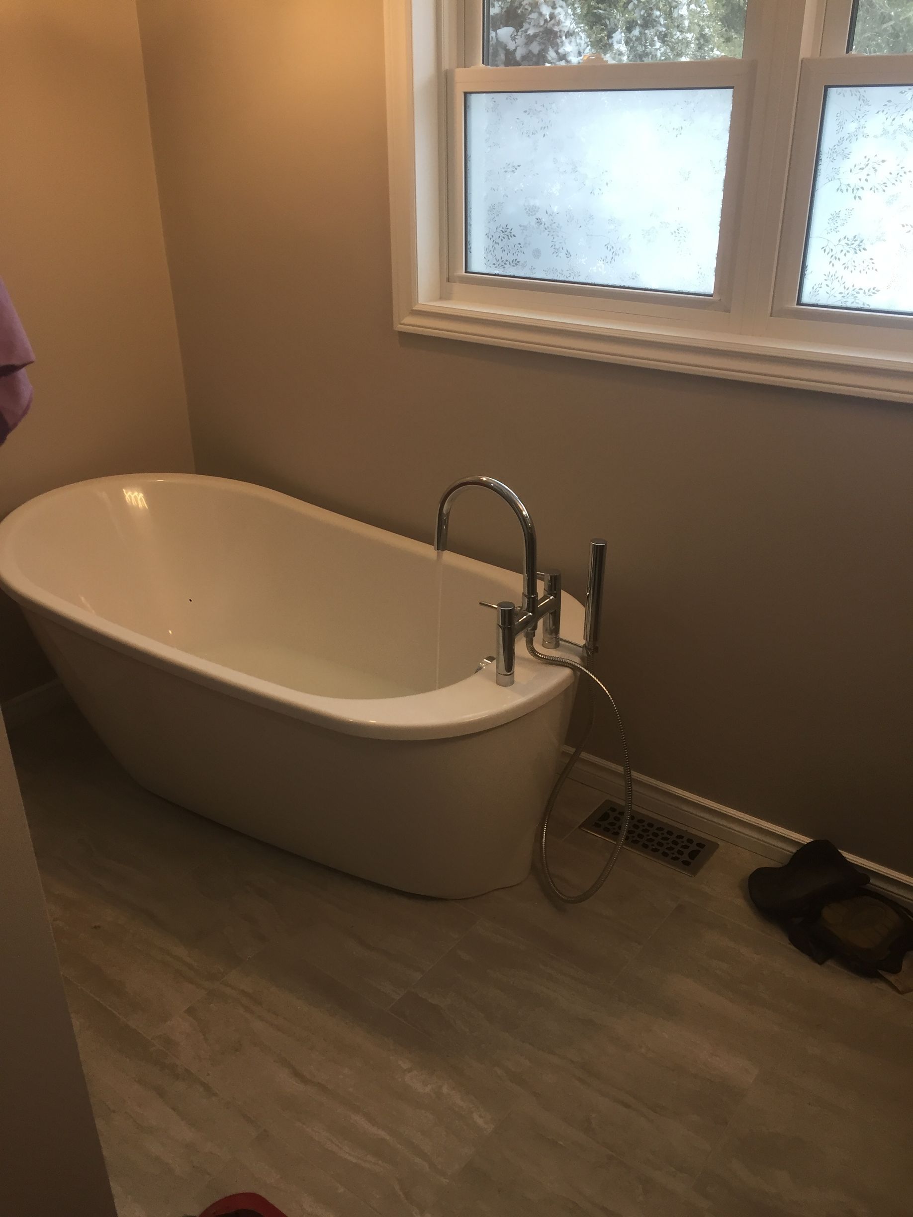 Oval freestanding bathtub in a bathroom with a window, beige walls, and light flooring.