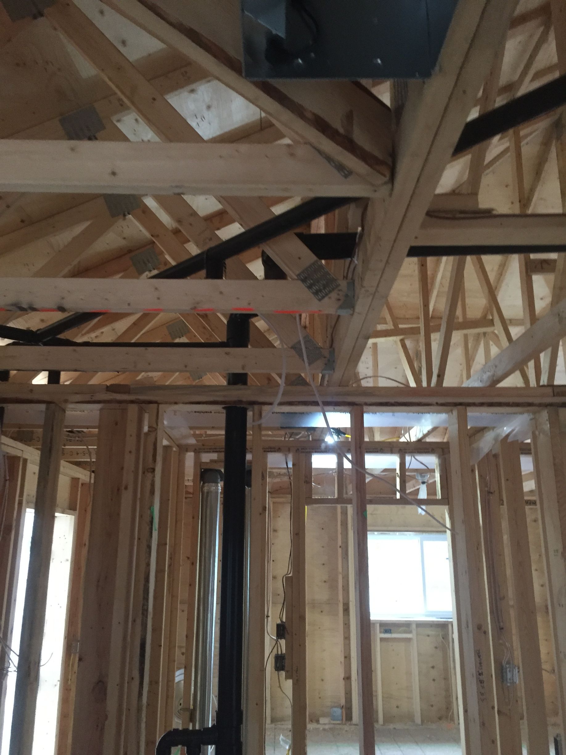 Interior framing of a house under construction, with exposed wooden beams, pipes, and wiring.