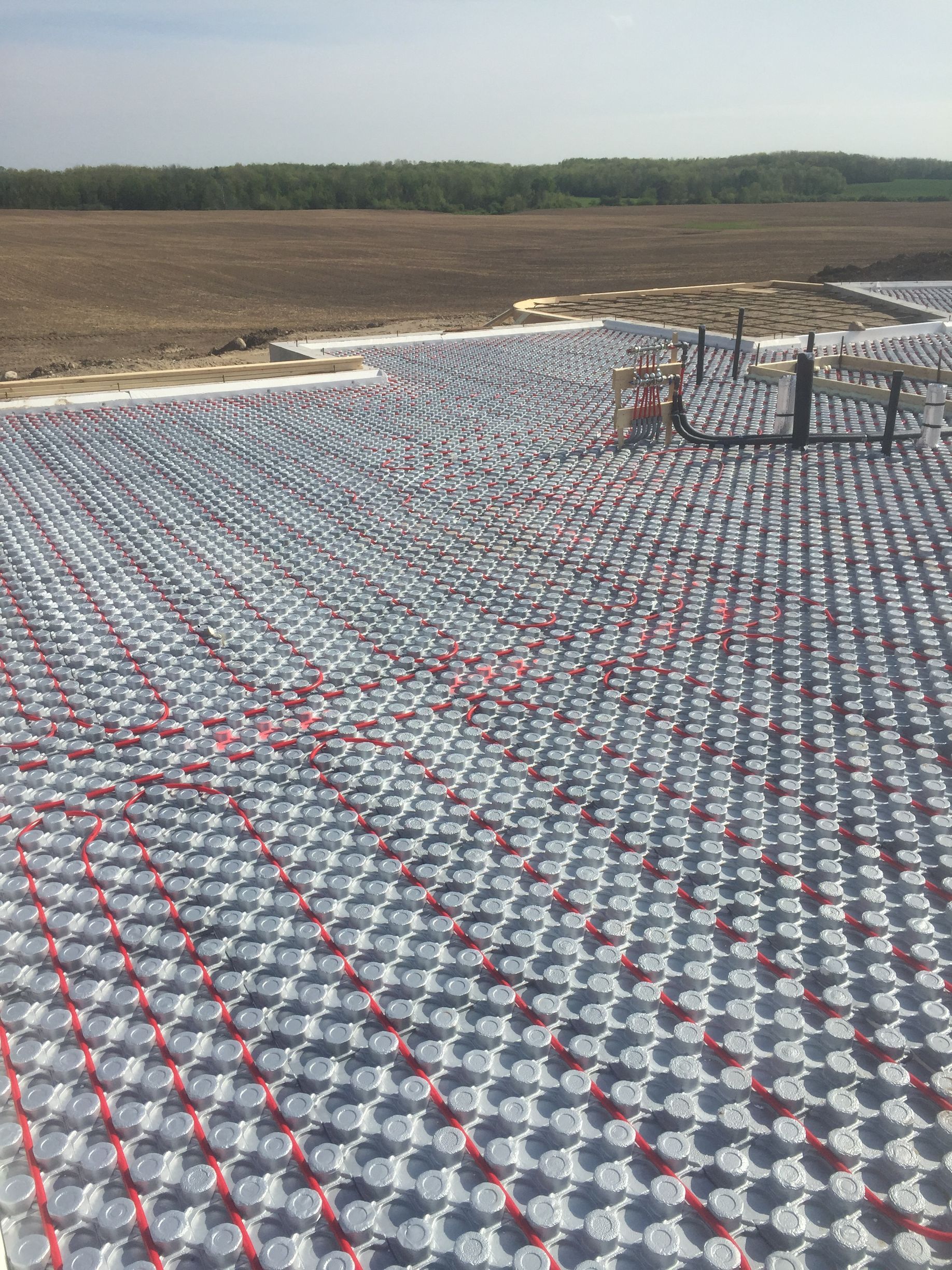 Red tubing laid on a gray grid for an in-floor heating system, prepared for concrete. Outdoors, construction site.