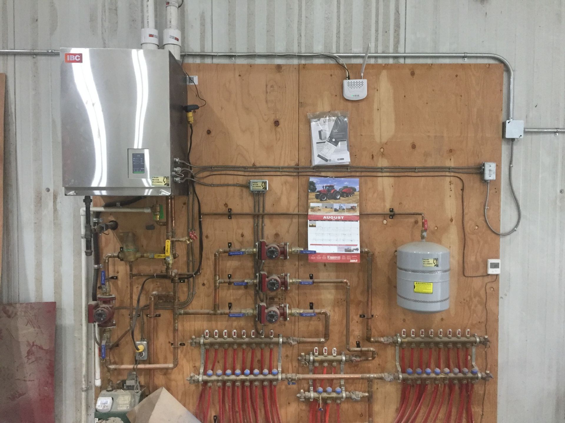 Stainless steel tankless water heater and radiant floor heating system mounted on plywood. Copper piping and red tubing.