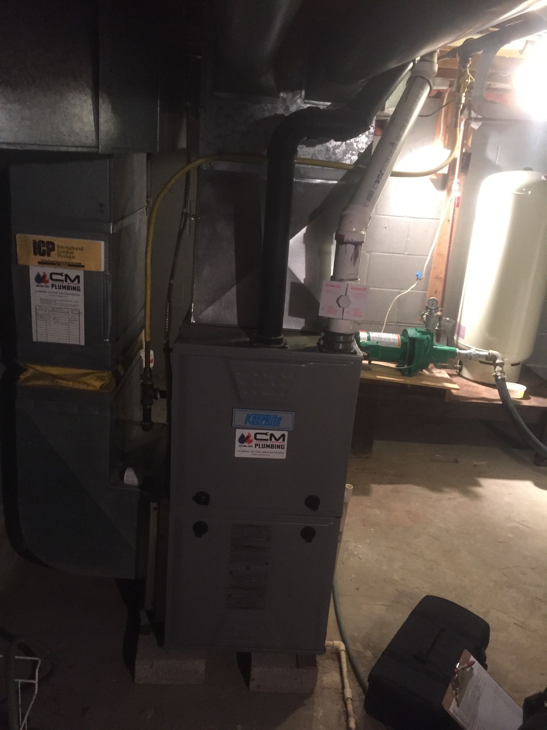 Furnace and air handler in a basement. Gray metal appliances with black vent pipes and plumbing visible.